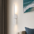 White wall-mounted tube sconce with a square base casts warm light beside curtains and a sofa.