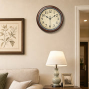 A vintage round wall clock with a cream face and dark wood frame above a side table.