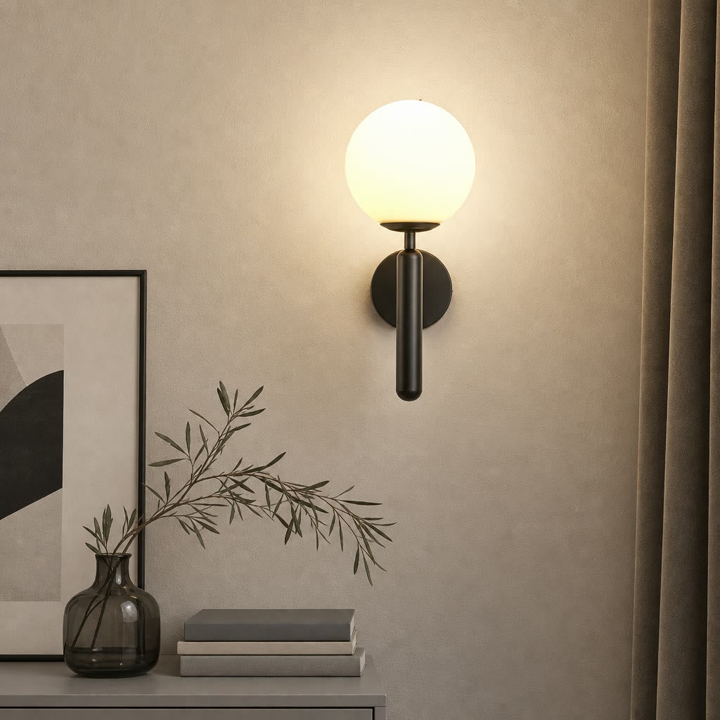 Black wall sconce with glowing white globe mounted above a console with books and a vase.