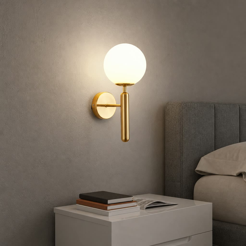 Gold wall sconce with glowing white globe above a white bedside table near a gray upholstered bed.