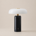 Glossy black cylindrical table lamp with a white rounded shade and brass accents.