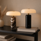 Two mushroom table lamps with cream shades, brass stems, marble and black cylindrical bases.