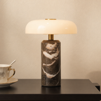 Glossy white and brass lamp with a dark marble cylinder base on a side table.