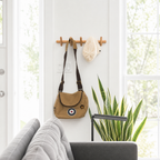 Wooden wall rack with rounded pegs holding a bag and knit hat between bright windows.