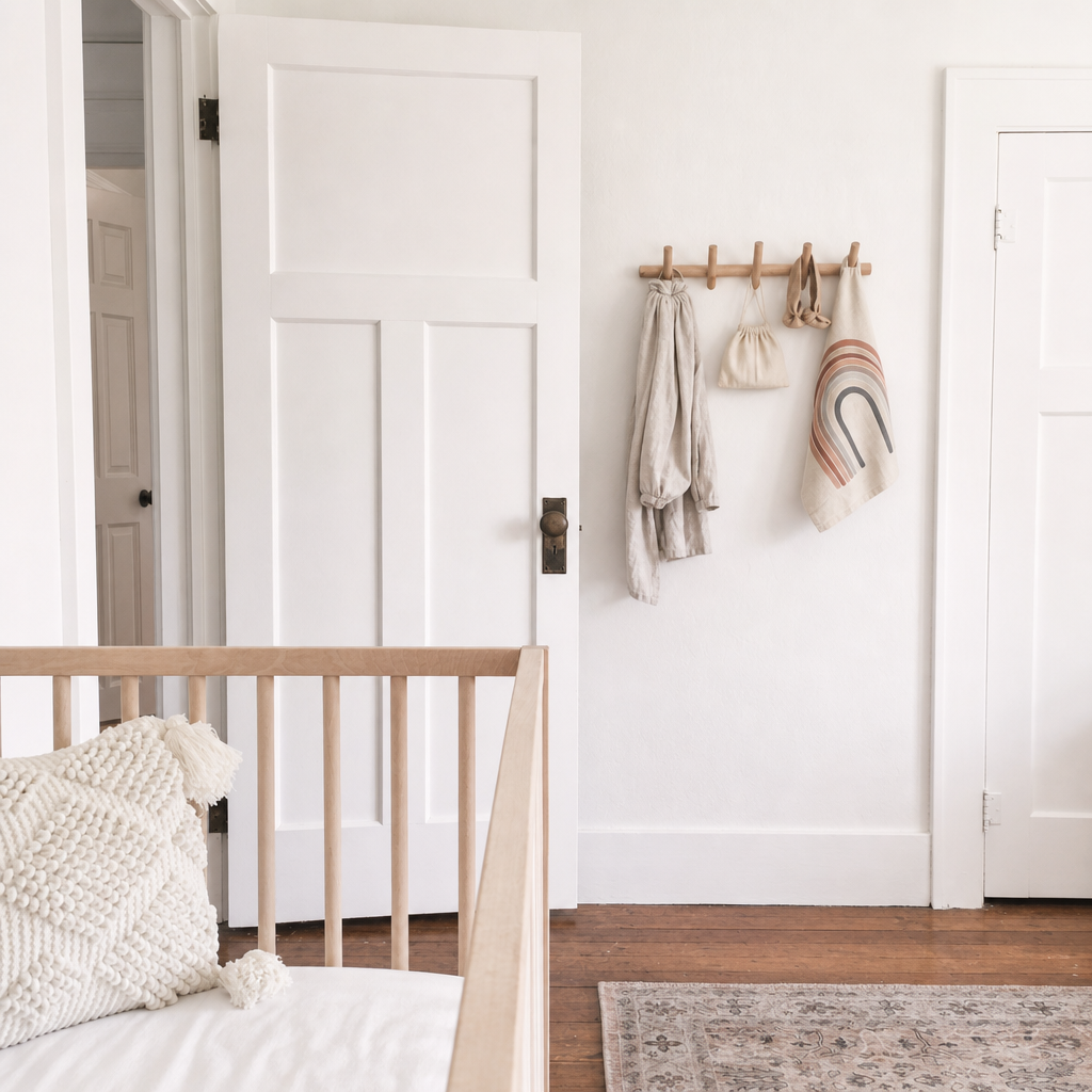 White paneled door beside a wooden peg rail with hanging bags and a rainbow wall charm.