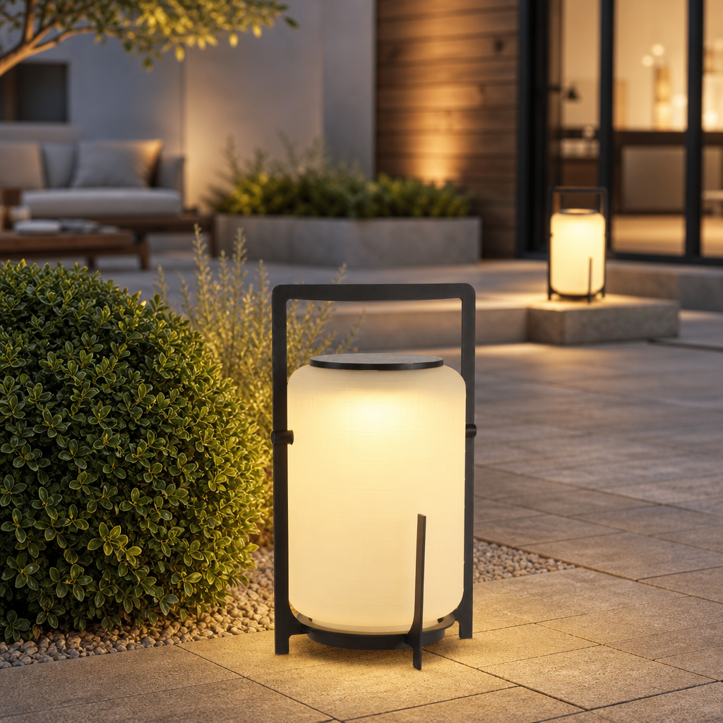 Glowing black-framed outdoor lantern on a modern patio beside shrubs and stone steps.