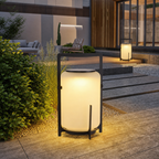 Glowing cylindrical outdoor lantern with black metal frame on a modern garden patio.