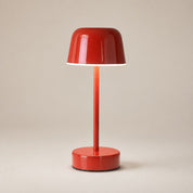 Glossy red cordless table lamp with dome shade and round base on a warm neutral backdrop.