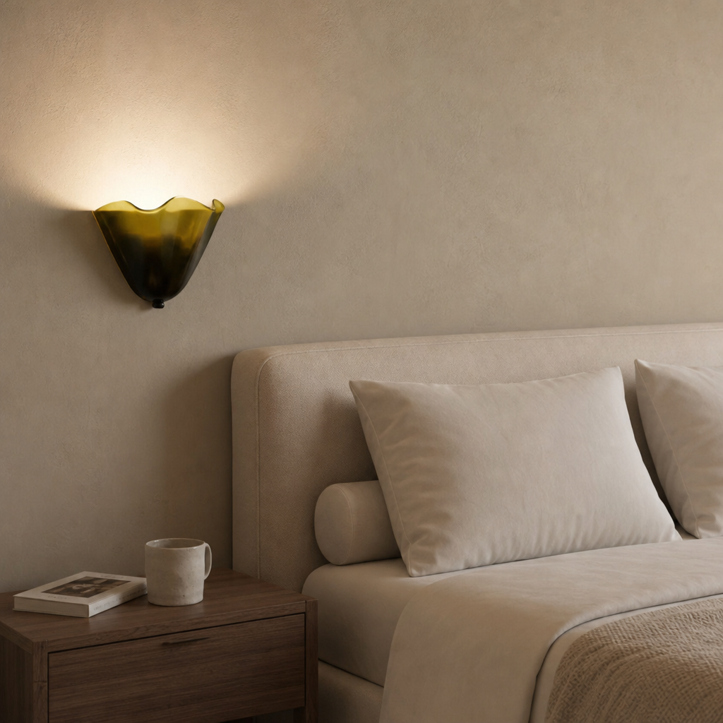 Amber glass wall sconce glowing above a neutral bedside scene.