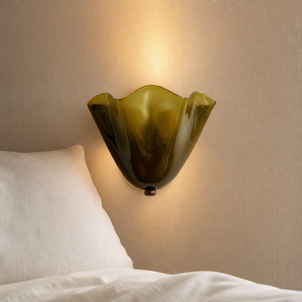 Olive green scalloped glass wall sconce glowing above white bedding.
