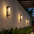 Three cylindrical ribbed wall lights glow warmly along a tiled outdoor garden wall.