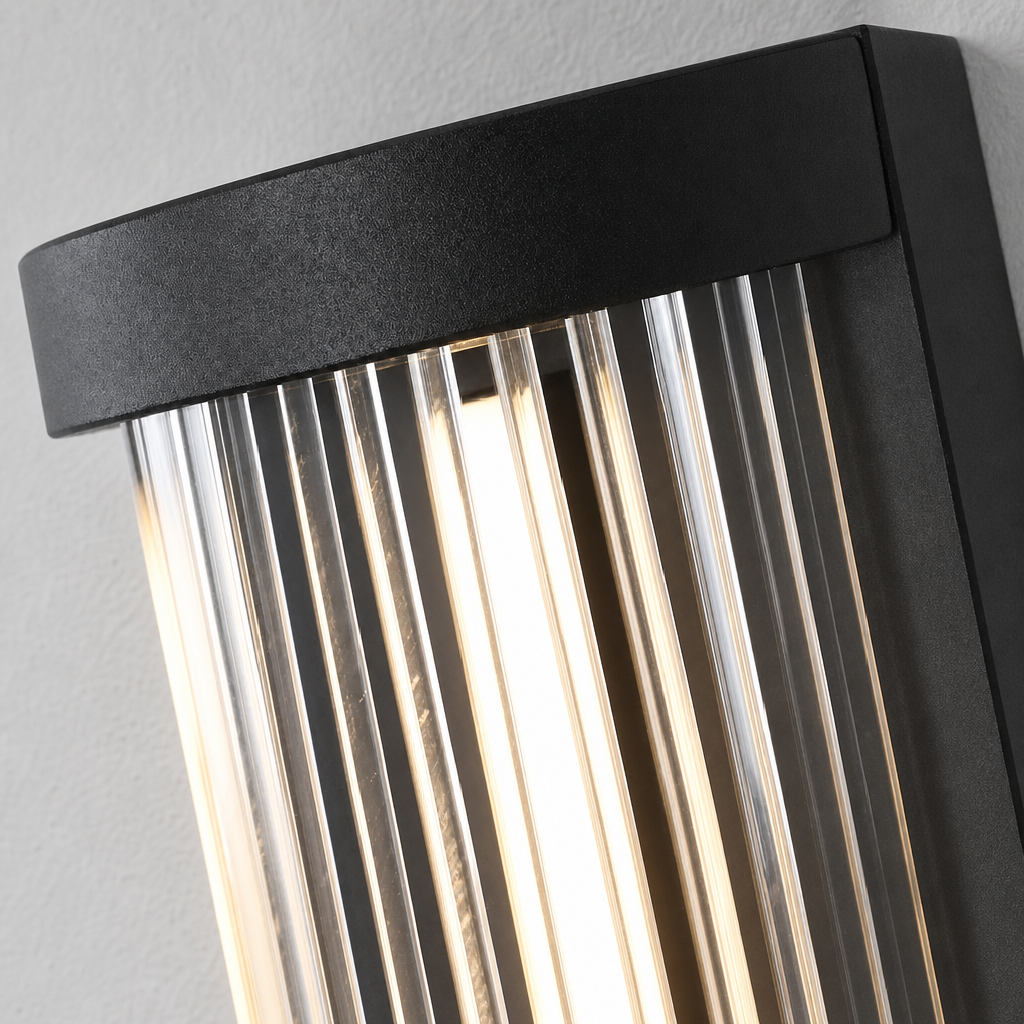 Black ribbed glass wall sconce glowing warmly against a light gray wall.