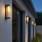 Black ribbed glass outdoor wall sconces glow warmly along a modern exterior wall.