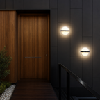 Modern circular wall lights on dark exterior panels beside a warm wooden entry door.