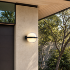 Glowing round outdoor wall sconce with a black horizontal band on a modern stucco exterior.