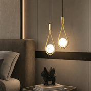 Two gold teardrop pendant lights with glowing round bulbs hang beside a bed headboard.