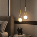 Two gold teardrop pendant lights with glowing round bulbs hang beside a bed headboard.