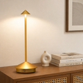Gold cordless table lamp with round base and slim stem on a wooden console.