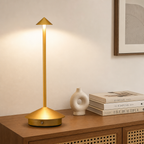 Gold cordless table lamp with round base and slim stem on a wooden console.