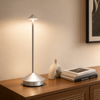 Silver touch table lamp with a slim pole and glowing cone shade on a wooden console.