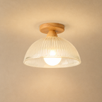 Warm wood flush mount ceiling light with a cream ribbed dome shade and glowing bulb.