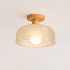 Woven beige ceiling light with wooden mount and glowing bulb on a plain light background.