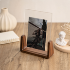 Clear acrylic photo frame in a wooden base displaying a portrait on a warm wooden desk.