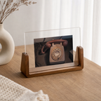 Clear acrylic photo frame with wooden base displaying a vintage rotary telephone on a sunlit wooden table.