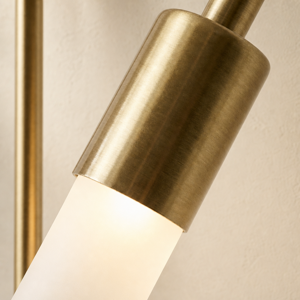 Brushed brass cylindrical lamp head with a glowing frosted tube against a neutral wall.