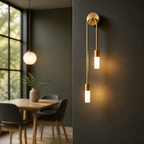 Brass double pendant wall sconce with two glowing cylindrical bulbs on a dark textured wall.