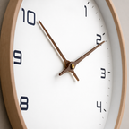 Close-up of a white wall clock with wood hands, black numerals, and a pale wooden frame.