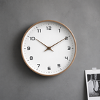 Round wall clock with a wood rim, white face, black numerals, and brown hands on a gray wall.