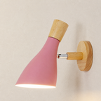 Pink cone wall sconce with wooden accents lit against a pale textured wall.