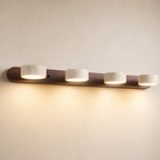 Four-light wall fixture with a wooden bar and cream stone shades glowing warm.