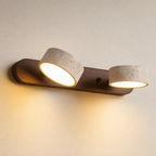 Two-light wall sconce with wood backplate and cream stone shades glowing warmly.