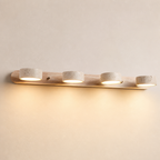 Four-light wooden vanity fixture with stone-textured round shades glowing warm on a pale wall.