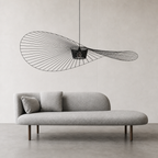 Gray rounded chaise sofa with two pillows beneath a sculptural black wire pendant light.