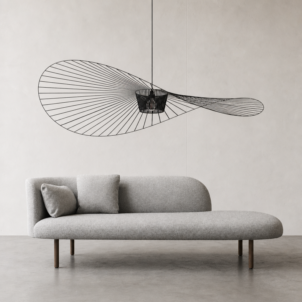 Gray rounded chaise sofa with two pillows beneath a sculptural black wire pendant light.
