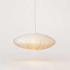 Warm oval ribbed paper pendant lamp with a white cord against a clean pale background.