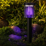 Black garden mosquito zapper lamp with a purple glow among grass and rocks.