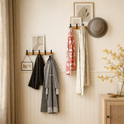 Wall-mounted wooden coat hook racks with black hooks holding coats, scarves, a hat, and framed decor.