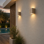 Two square stone wall sconces cast warm light on a textured exterior wall.