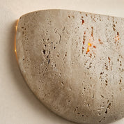 Beige porous stone wall sconce with warm light glowing through small openings.