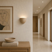 Speckled beige half-bowl wall sconce glowing on a warm neutral hallway wall.