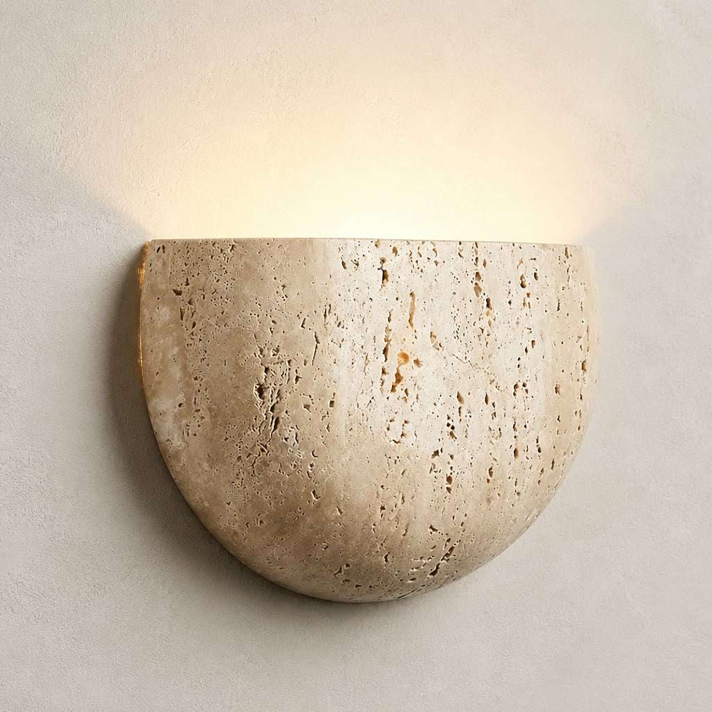 Beige semicircular stone wall sconce glowing softly on a pale textured wall.